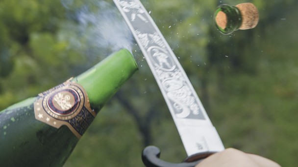Garrafa de espumante tendo sua ponta arrancada com um sabre.